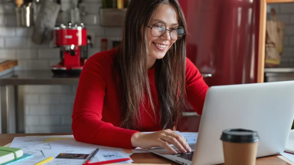 Mulher sorridente trabalhando em um computador, questionando o que é o Departamento Pessoal - DP. A imagem ilustra um ambiente profissional e moderno.