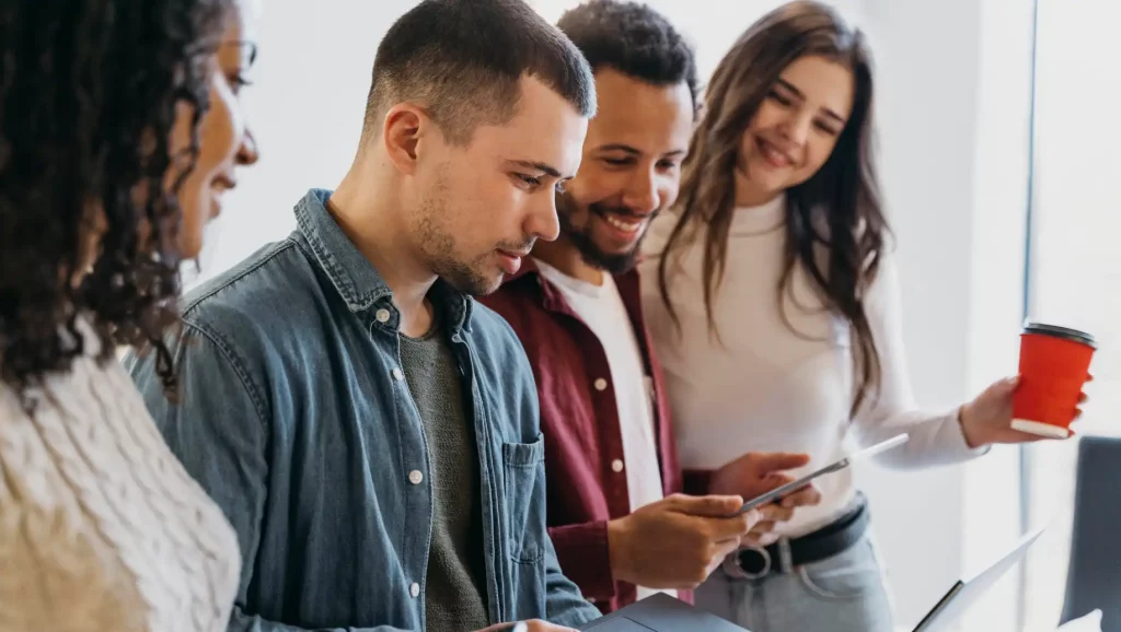 Grupo de jovens profissionais analisando conteúdo digital de engajamento no trabalho com dispositivos móveis em ambiente de trabalho colaborativo. Foco em tecnologia e interação.