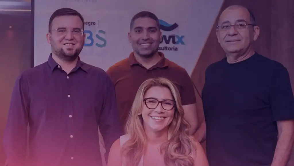 Grupo de quatro pessoas da Montenegro Contabilidade sorridentes em evento, incluindo duas mulheres e três homens, com fundo de banner de empresa e ambiente interno.