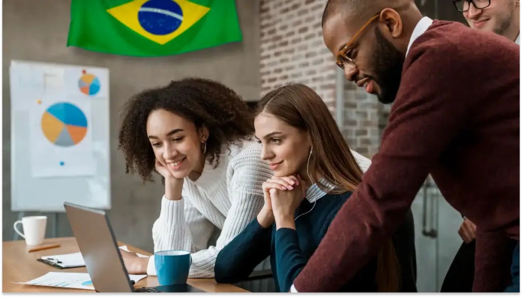 Grupo de jovens profissionais em uma reunião de trabalho, focados em um laptop, com o Brasil ao fundo, destacando o crescimento profissional e a colaboração. Imagem representando contratações.