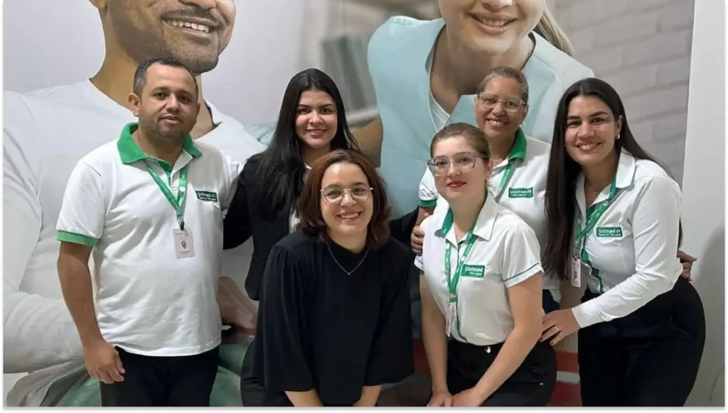 Grupo de profissionais sorridentes em ambiente corporativo, vestindo uniformes com logotipo e identidades diversas, promovendo colaboração e trabalho em equipe.