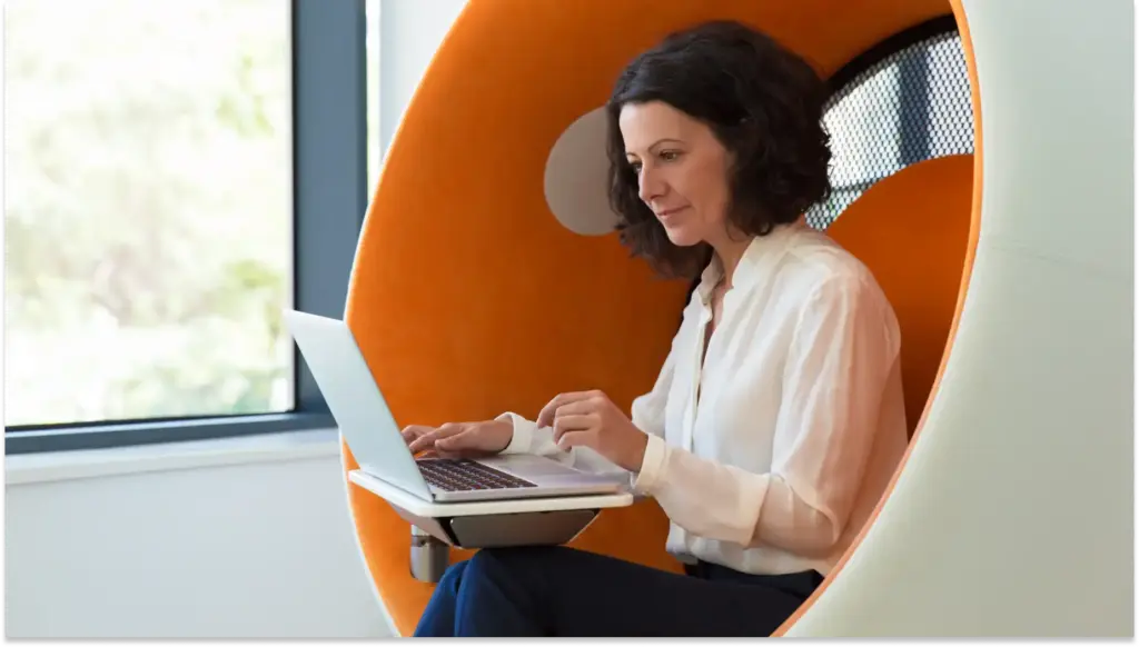 Mulher usando laptop em um espaço de coworking moderno, com IA no RH e design inovador e ambiente de trabalho acolhedor, ideal para criatividade.