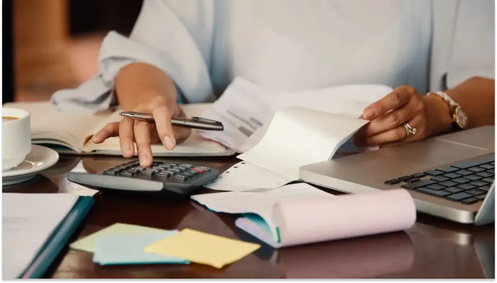 Pessoa trabalhando com documentos, usando calculadora para calcular a isenção do imposto de renda, laptop e caneta em uma mesa de escritório, com foco em tarefas administrativas ou financeiras