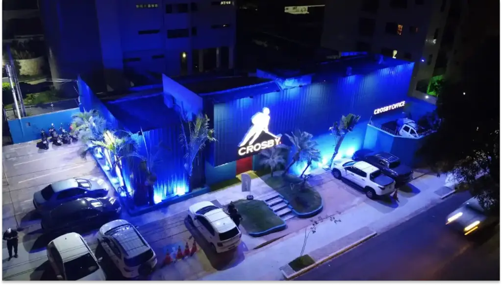 Iluminação azul da academia Crossfy em um bairro, com decoração de luzes, estacionamento com carros e árvores ao redor, vista noturna