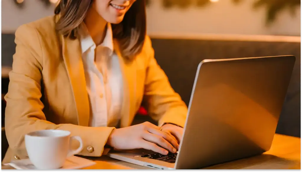 Mulher de negócios trabalhando no laptop em um ambiente aconchegante, com uma xícara de café ao lado, representando RH 2026, produtividade e empreendedorismo.