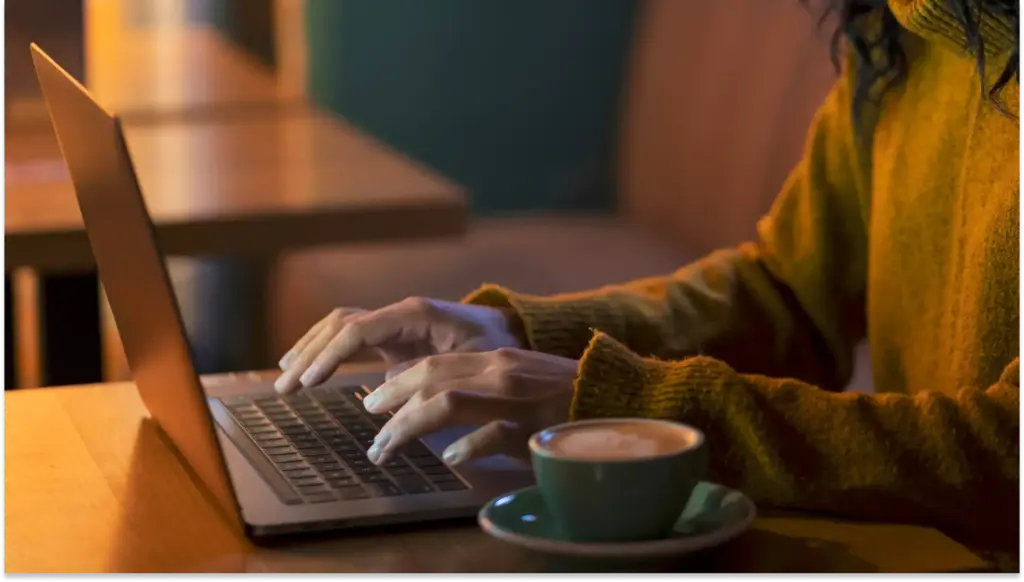 Pessoa usando laptop no trabalho remoto e tomando café em ambiente aconchegante, ideal para trabalho remoto ou estudos em casa.