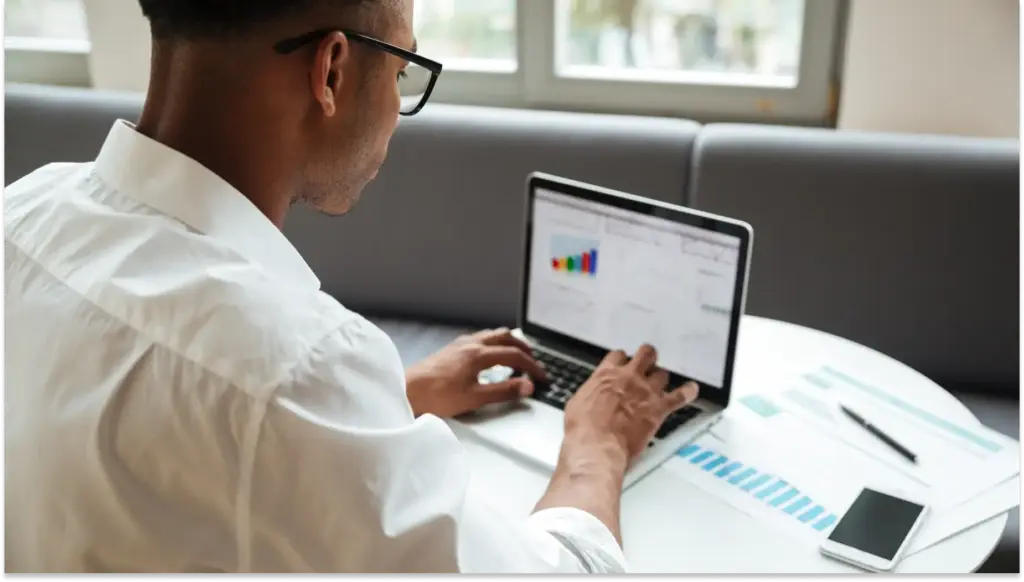 Homem de óculos analisando gráficos de dados DA Nova tabela do IRPF em seu laptop durante trabalho em ambiente de escritório.