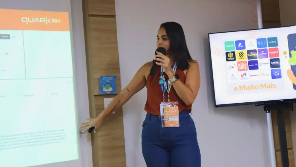 Palestrante durante workshop de Gestão de Pessoas de Alta Performance, apresentando insights ao lado de telão com slide e audiência em evento corporativo.
