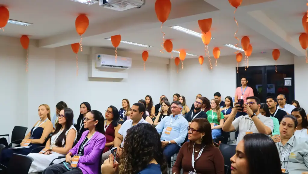 Público em workshop sobre Gestão de Pessoas de Alta Performance: insights, em sala de treinamento com profissionais sentados e balões laranja decorando o ambiente.