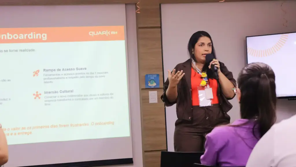 Workshop de Gestão de Pessoas de Alta Performance: insights. Palestrante em sala com telão exibindo slide sobre onboarding, enquanto apresenta para participantes sentados.