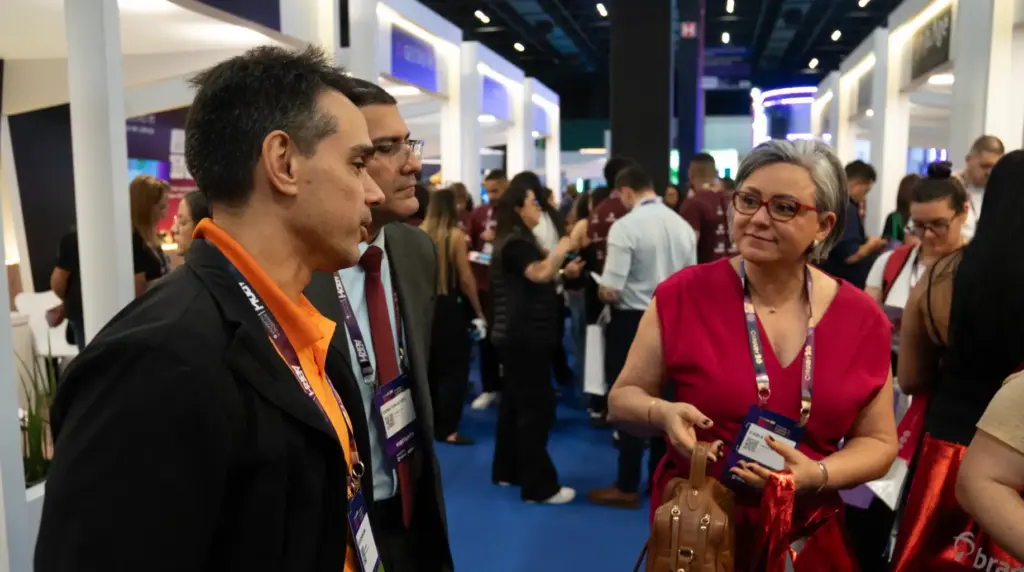 QuarkRH participa da 52ª edição do CONARH em SP: Profissionais conversam em um estande durante o evento, com crachás e comunicação em feira de negócios. Ambiente de congresso em SP.