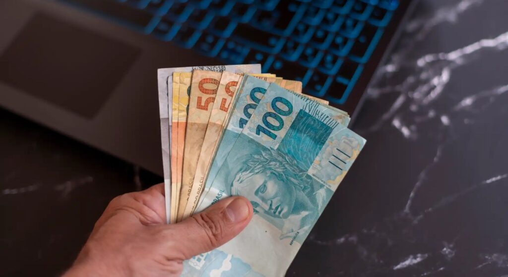 Pessoa calculando o décimo terceiro salário usando uma calculadora, com papéis e caneta em uma mesa de escritório.