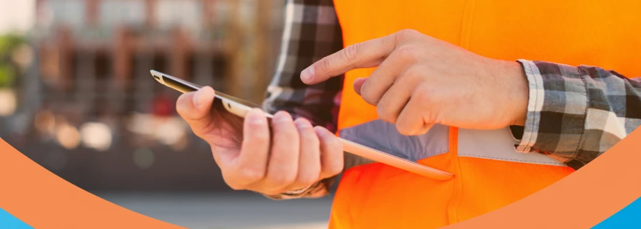 Homem com colete refletivo usando celular em um ambiente de construção. Importante para empresas brasileiras que deverão focar na avaliação de riscos psicossociais a partir de 2025.