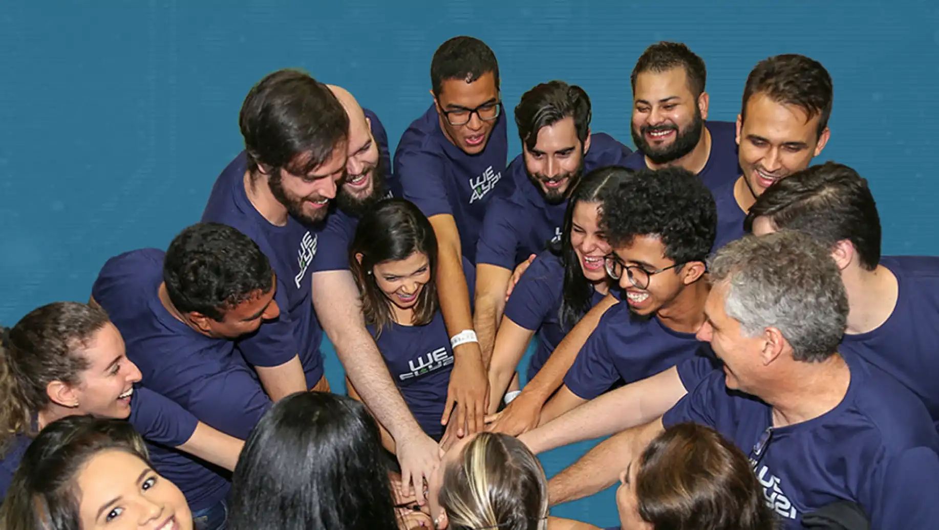 Grupo da P21 Sistemas celebrando e sorrindo com as mãos juntas, demonstrando união e trabalho em equipe.
