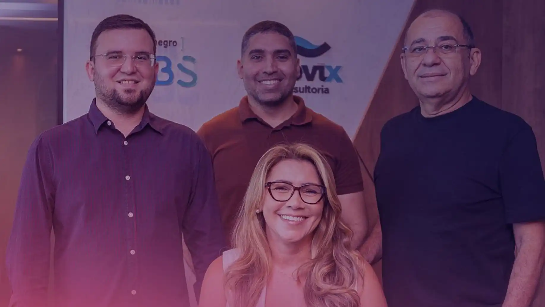 Grupo de quatro pessoas da Montenegro Contabilidade sorridentes em evento, incluindo duas mulheres e três homens, com fundo de banner de empresa e ambiente interno.