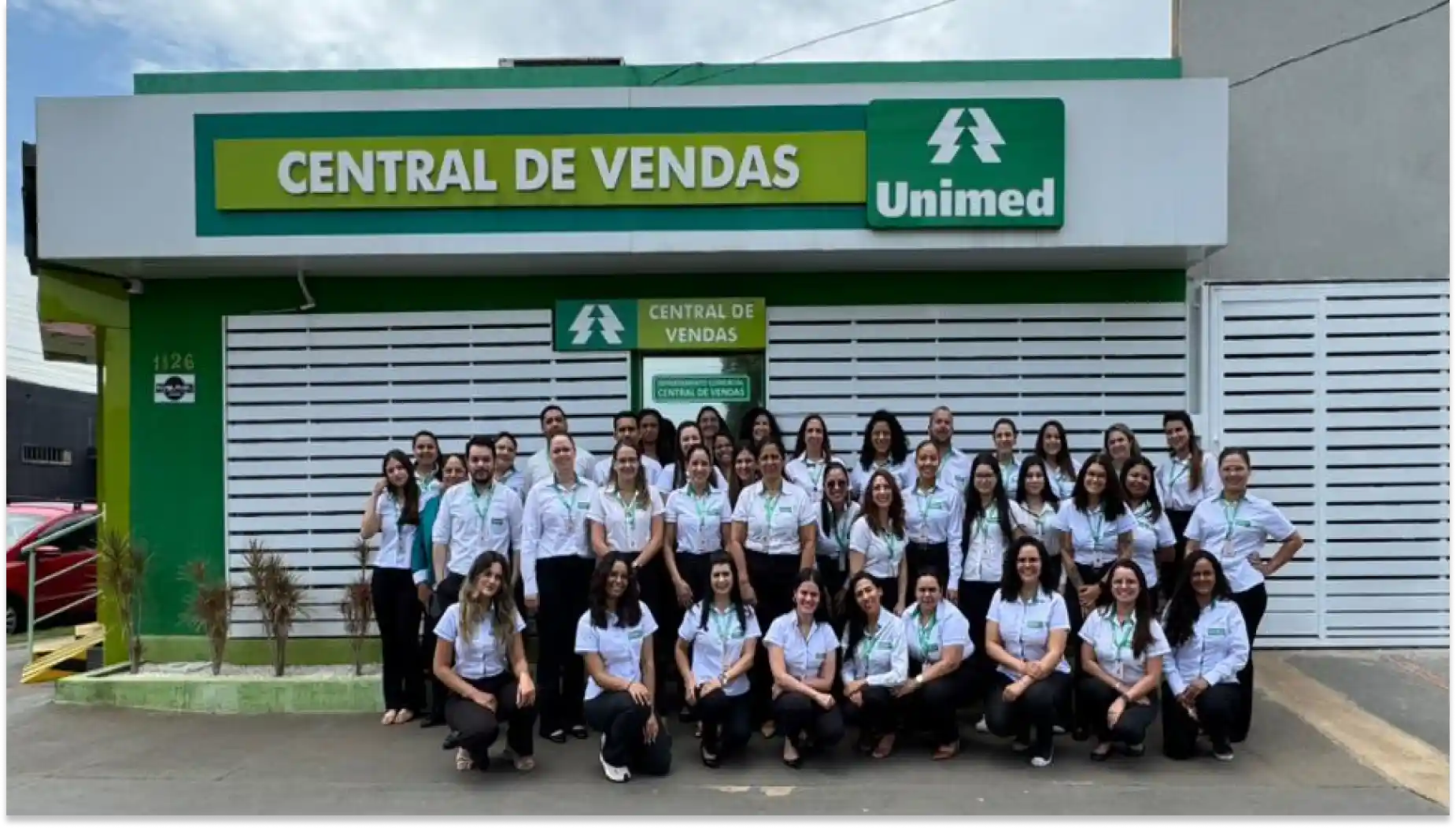 Grupo de profissionais sorridentes em ambiente corporativo, vestindo uniformes com logotipo e identidades diversas, promovendo colaboração e trabalho em equipe Unimed Três Lagoas