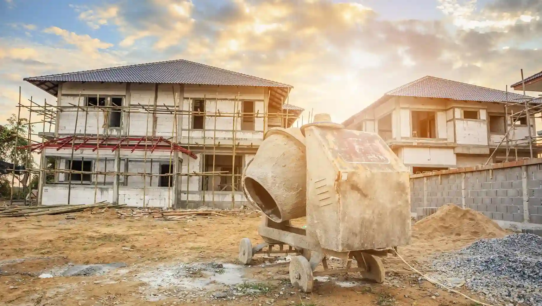 Construção de B&B Engenharia e Construções de casas residenciais em andamento com concreto e escavações no local, céu com nuvens ao entardecer.