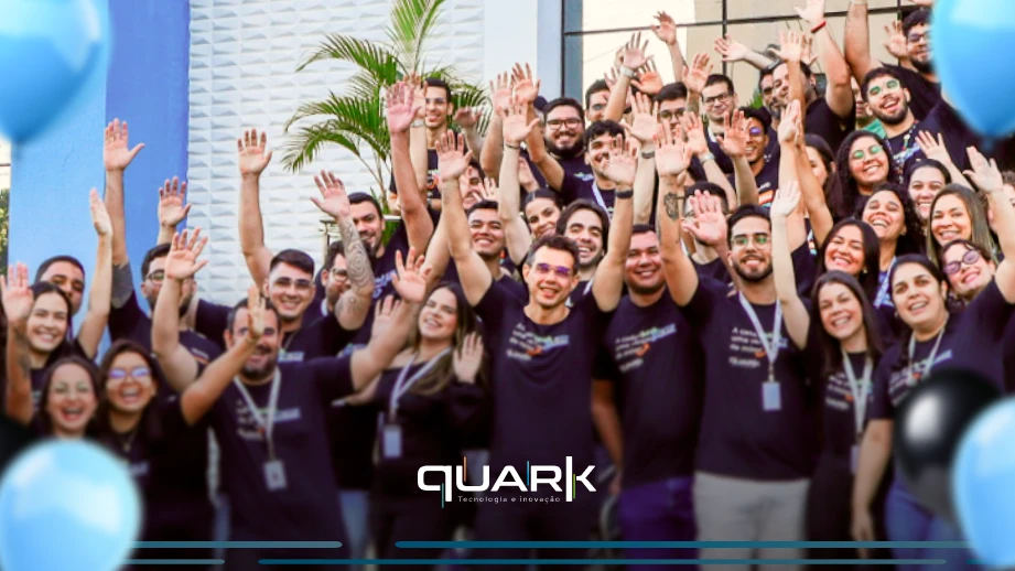 Grupo de funcionários da Quark Tecnologia e Inovação comemorando com sorriso e entusiasmo em evento corporativo, usando camisetas pretas e participando de celebração na empresa, comemorando os 1 mil clientes.