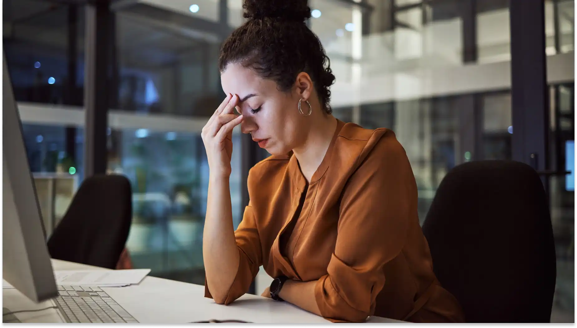 Mulher com expressão de preocupação e frustração, sentada em uma mesa de escritório com computador portátil, lidando com dificuldades da implementação da nova NR-01.