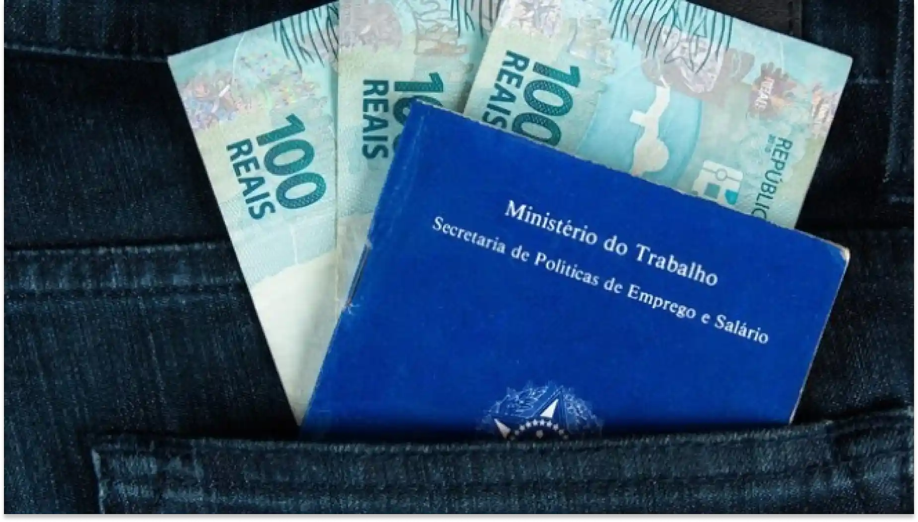 Dinheiro de 100 reais para representar o salário mínimo e documento do Ministério do Trabalho no bolso de uma calça jeans.