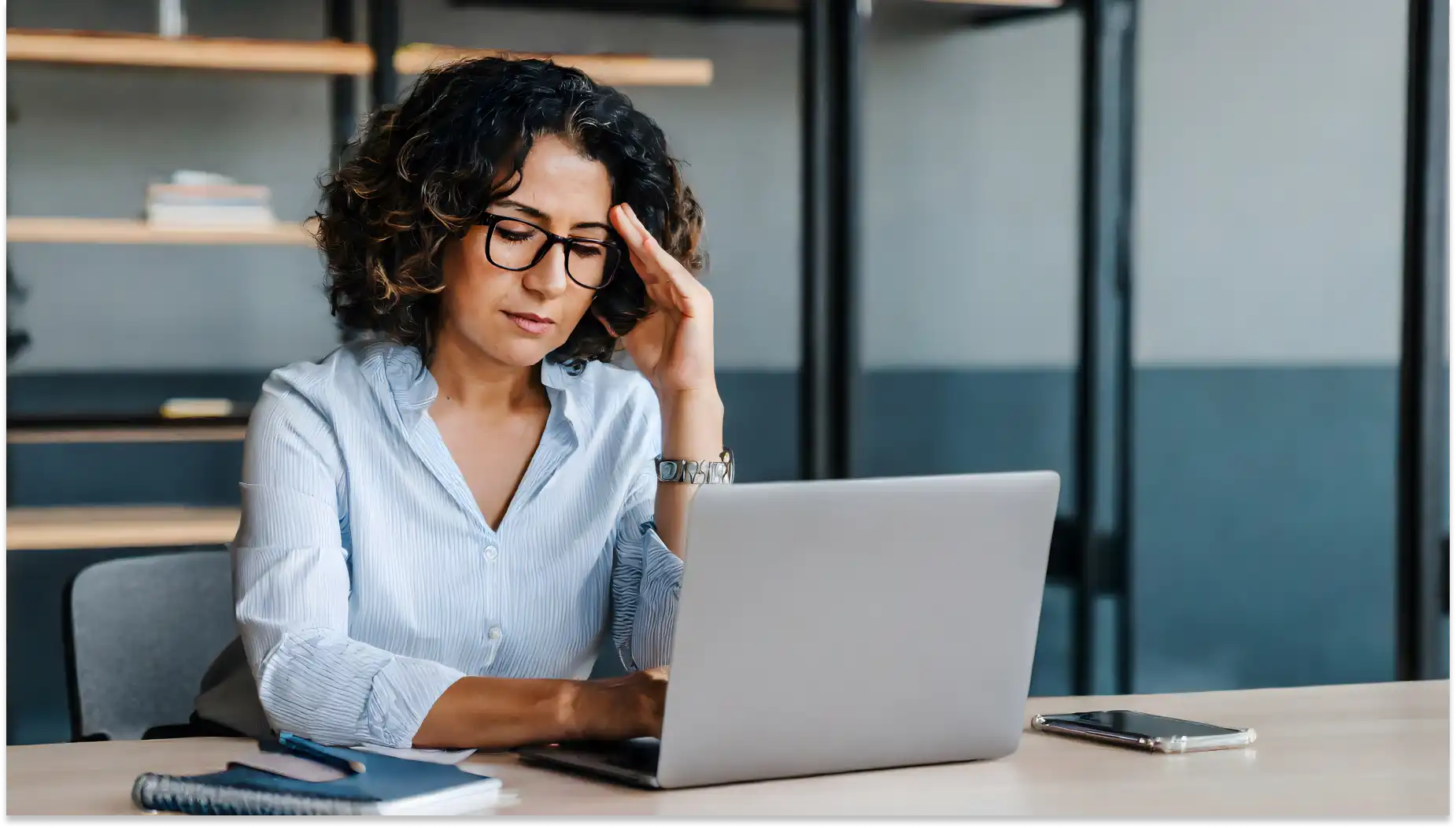 Mulher de escritório com óculos, expressão preocupada, sentada diante de um laptop, analisando impactos da IA no ambiente de trabalho.