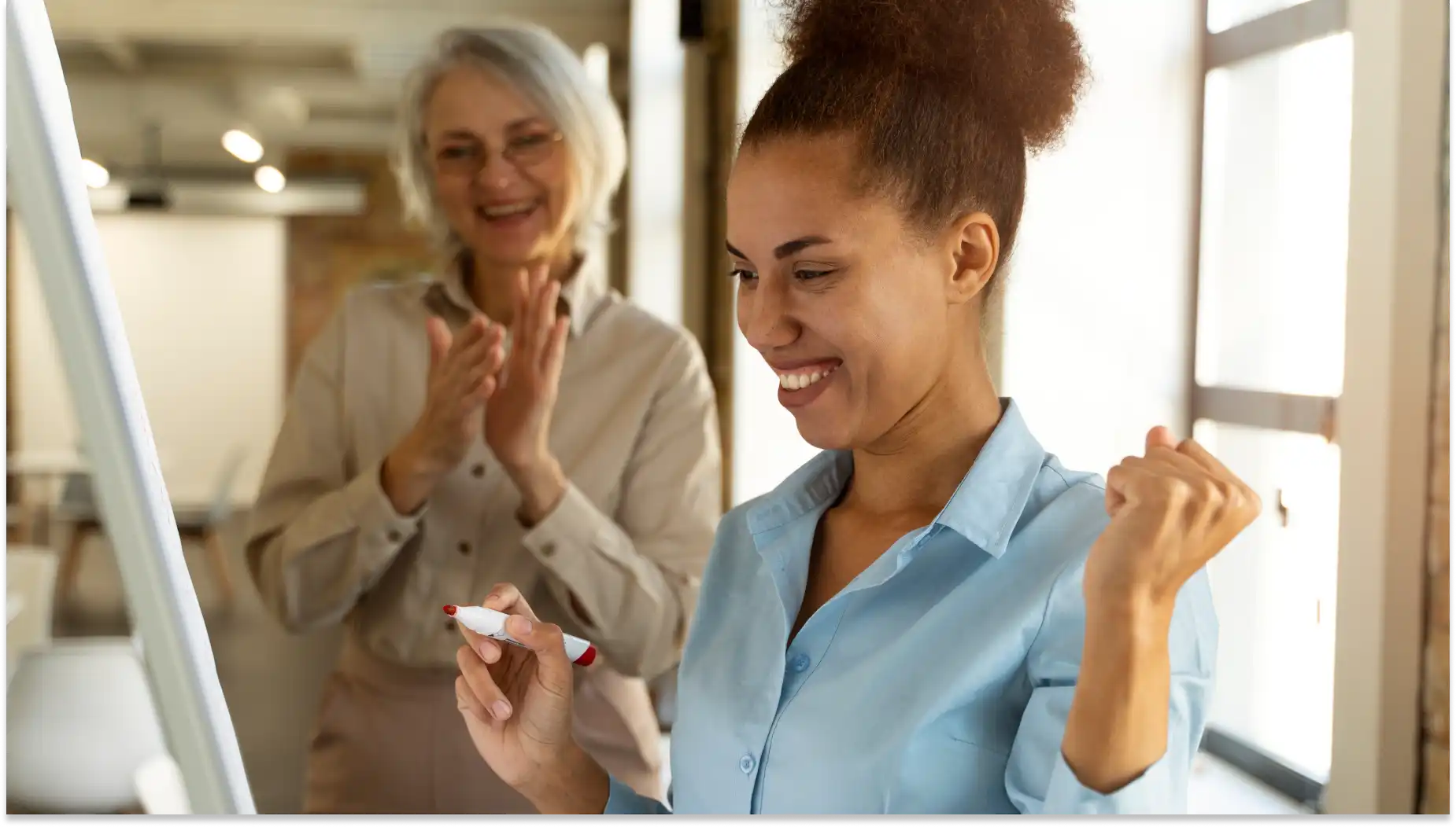 Mulher jovem comemorando benefícios personalizados ao lado de mulher mais velha, ambas sorrindo na frente de um computador em um ambiente de escritório.
