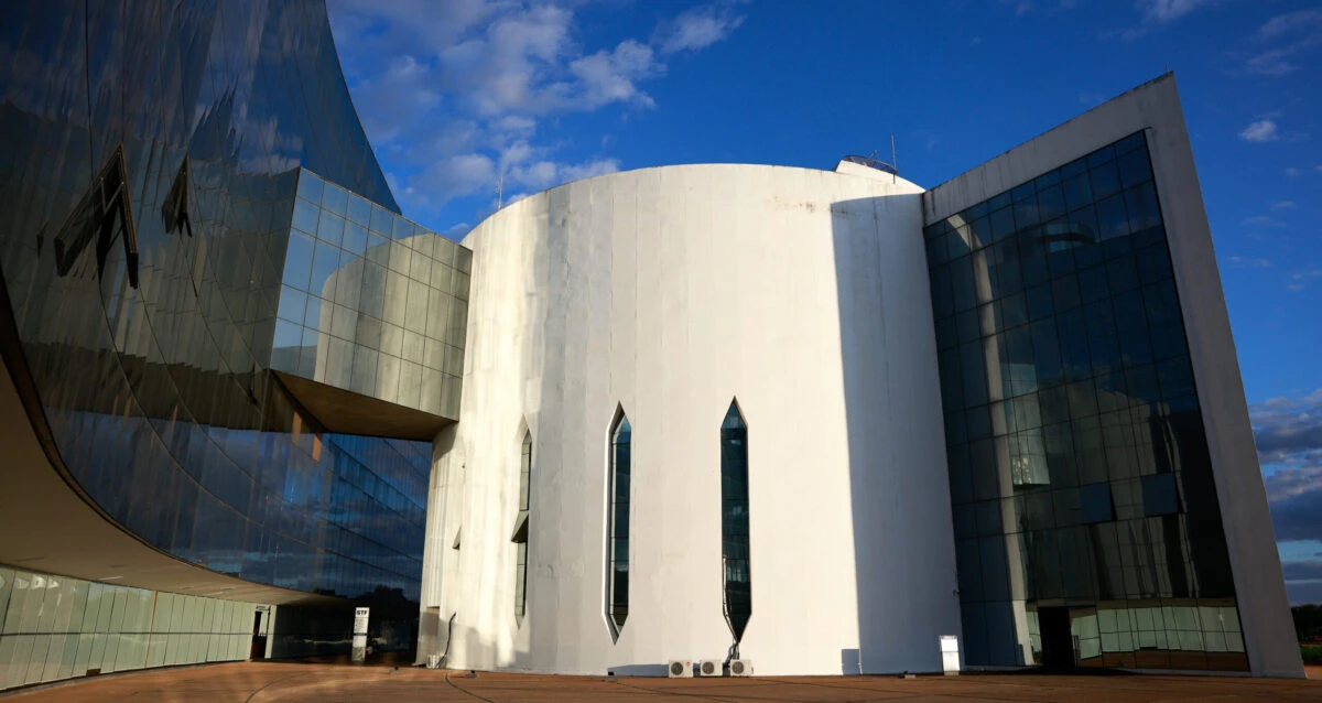 Prédio do Supremo Tribunal Federal (STF) com fachada moderna de concreto e vidros ao ar livre, sob céu azul com nuvens, cenário de decisão judicial