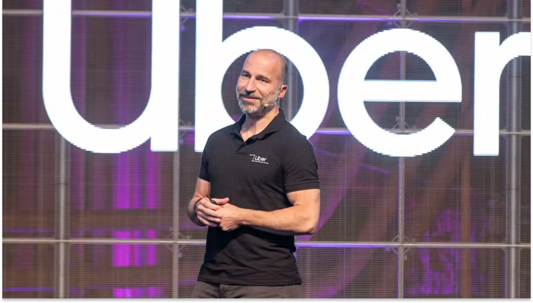 Imagem do executivo da Uber em palco, falando durante apresentação com o logotipo da empresa ao fundo, em contexto de anúncio de reestruturação e redução do time de RH e recrutamento em 23%.
