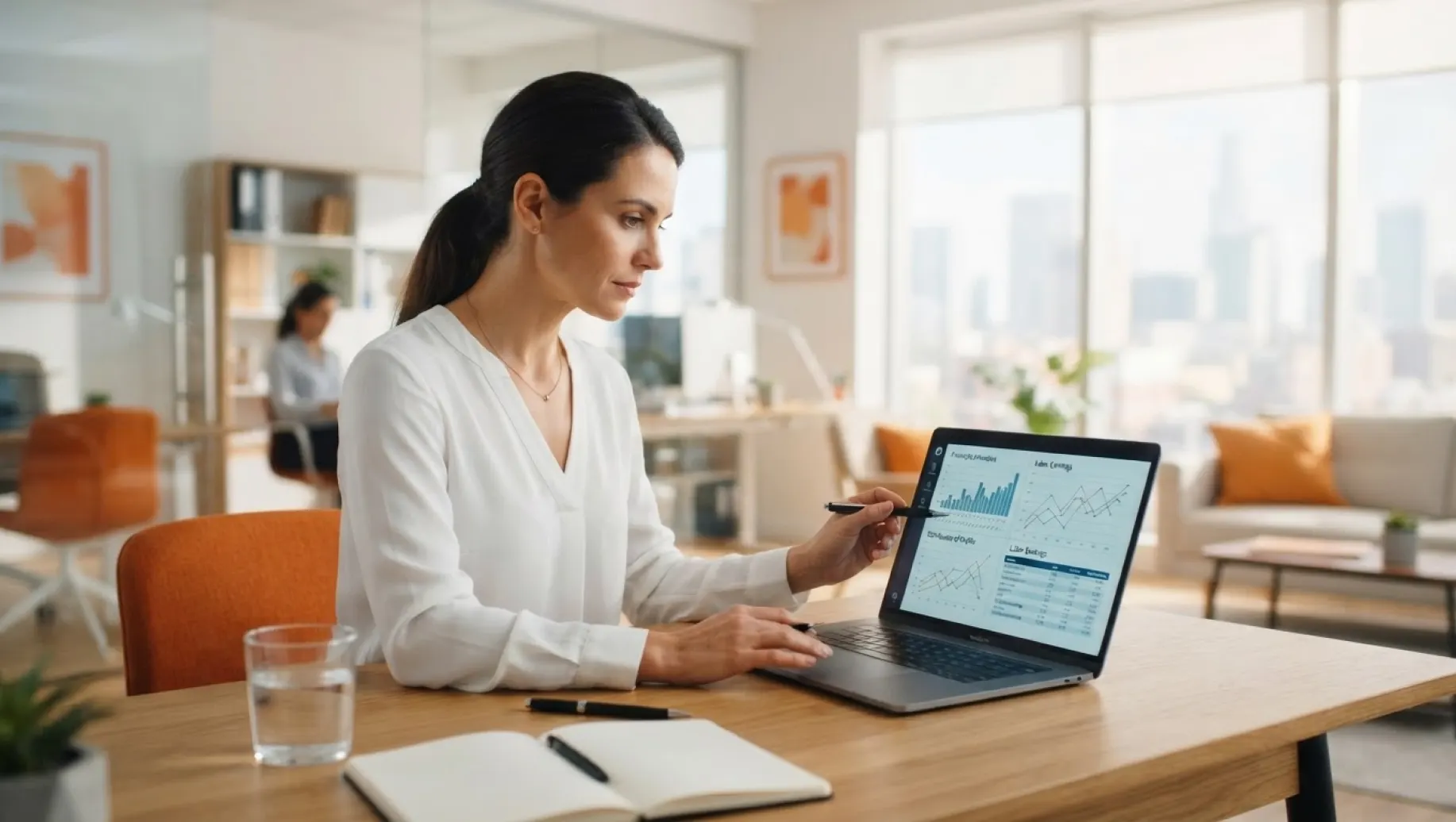 Mulher analisando gráficos financeiros em um notebook no escritório moderno, apontando dados de desempenho enquanto discute estratégias para aumentar o lucro com a equipe ao fundo.