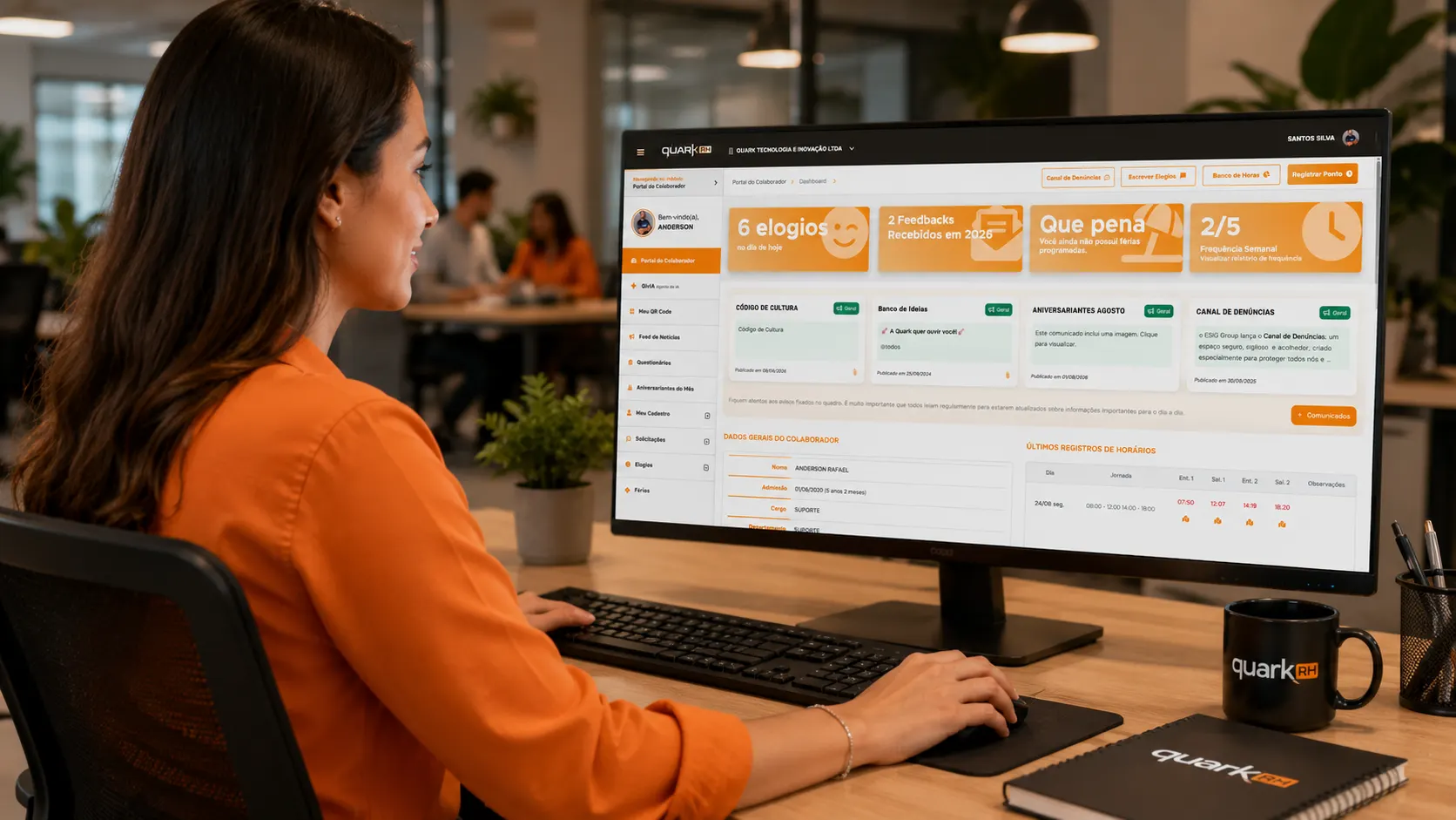 QuarkRH vs Convenia: Mulher trabalhando em escritório diante de um monitor com dashboard de sistema e xícaras com logotipo QuarkRH, enquanto utiliza teclado e mouse.