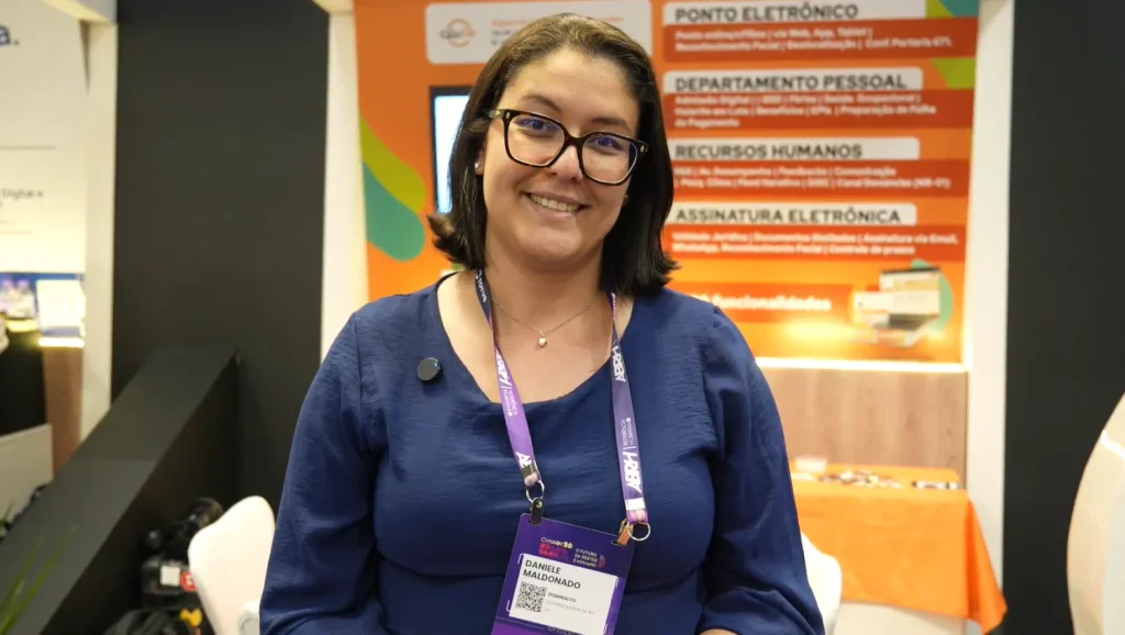 Dominalog: Foto de uma profissional sorrindo em evento corporativo, com crachá e cordão de identificação, ao lado de um banner com seções como departamento pessoal, recursos humanos e assinatura eletrônica.